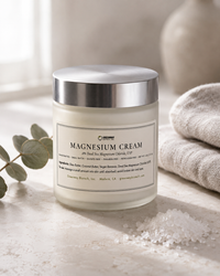 Magnesium Cream jar on pale stone with magnesium chloride flakes, a folded linen towel and eucalyptus